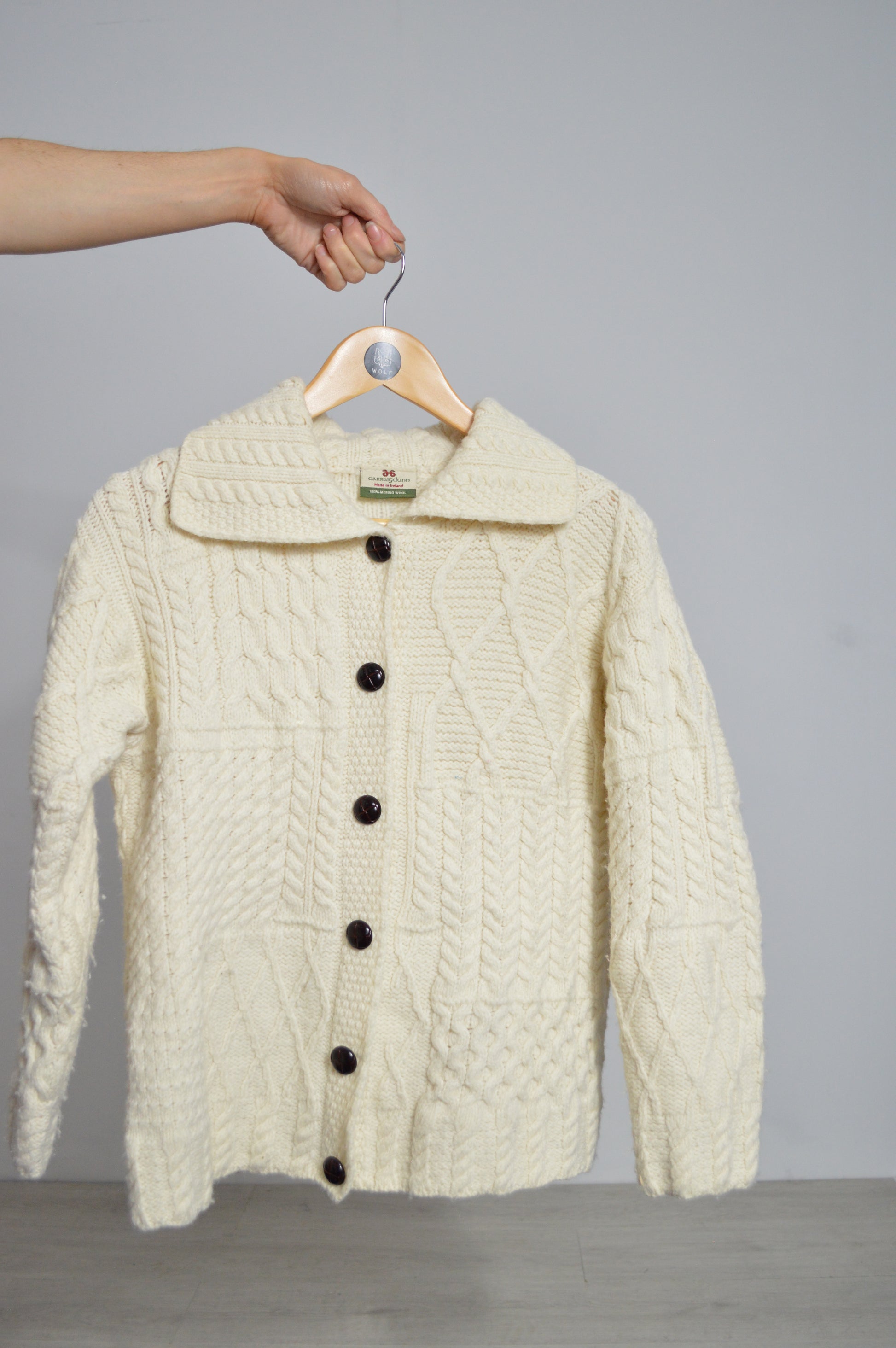 Knitted white bag with a face design held by a hand against a gray background